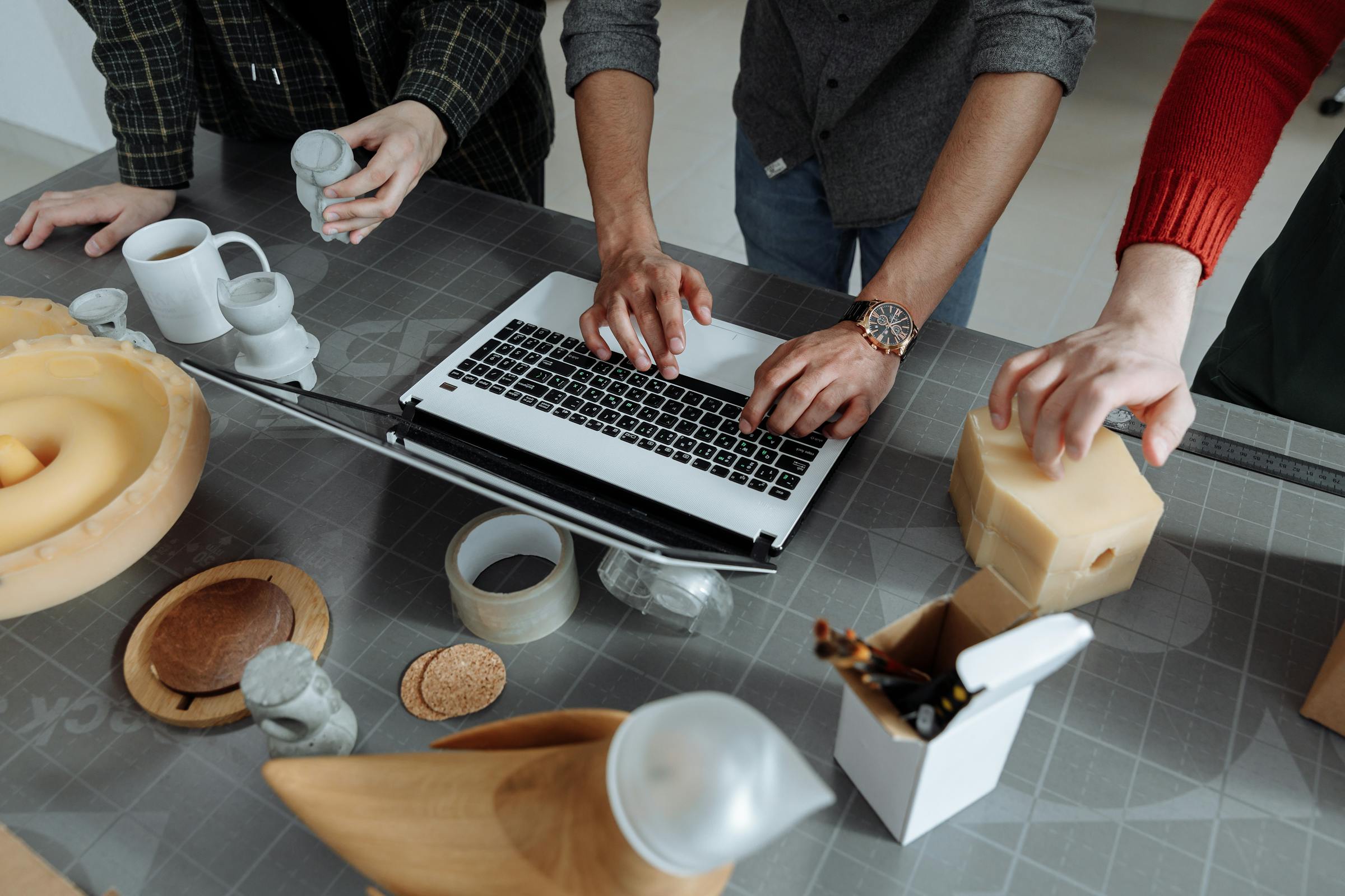 Hands arranging product design materials beside a laptop during a collaborative workshop.
